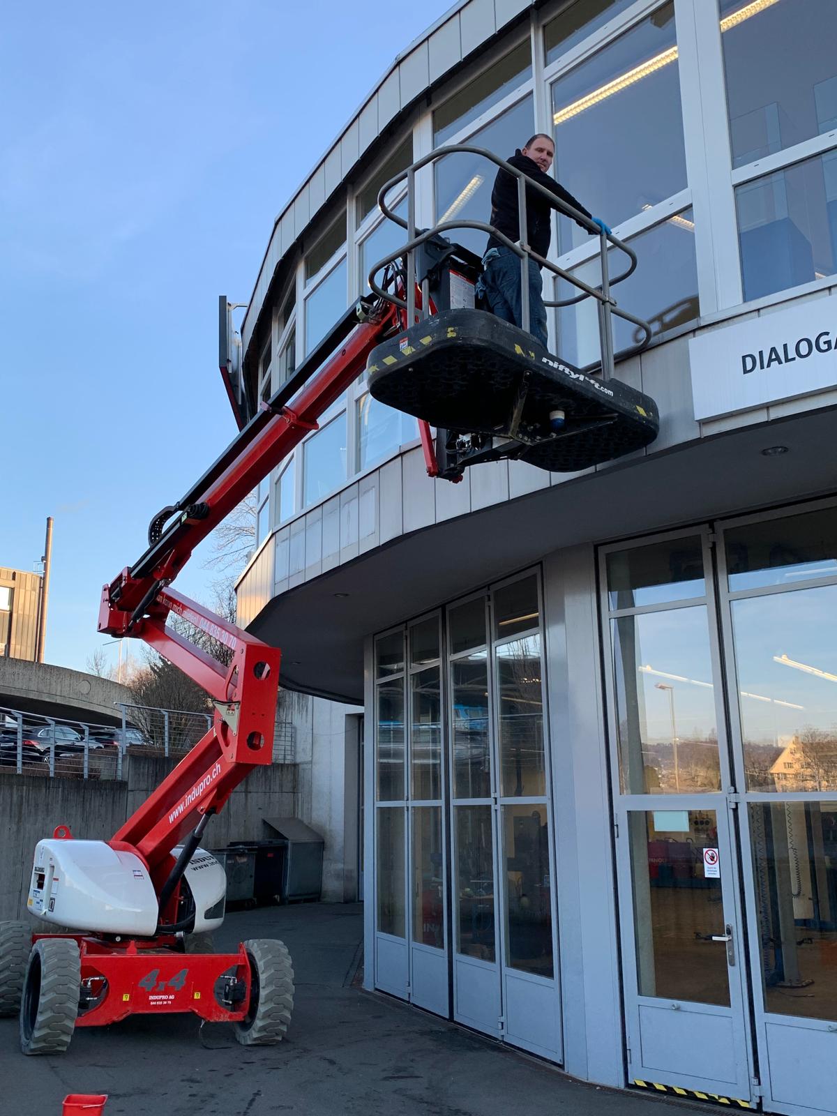 Mitarbeiter auf einer roten Hebebühne vor einer Glasfassade